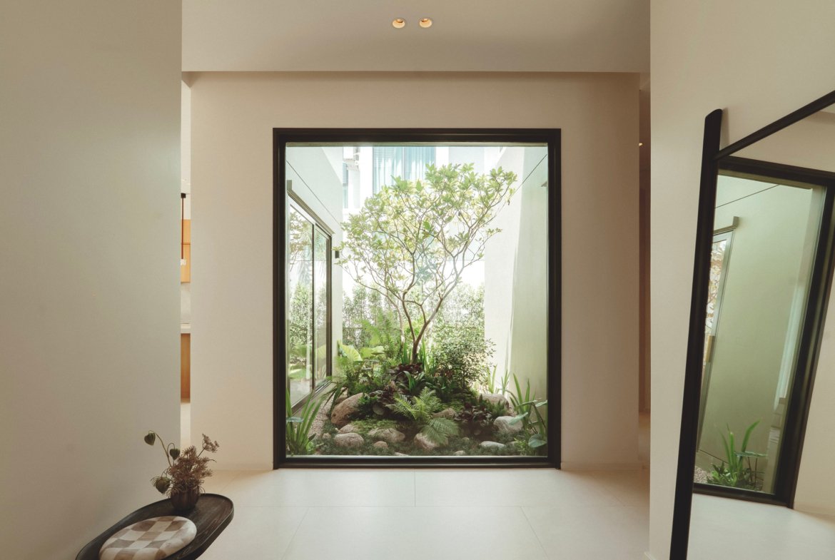 Interior hallway opening to a bright glass-walled courtyard with a tree and greenery outside.
