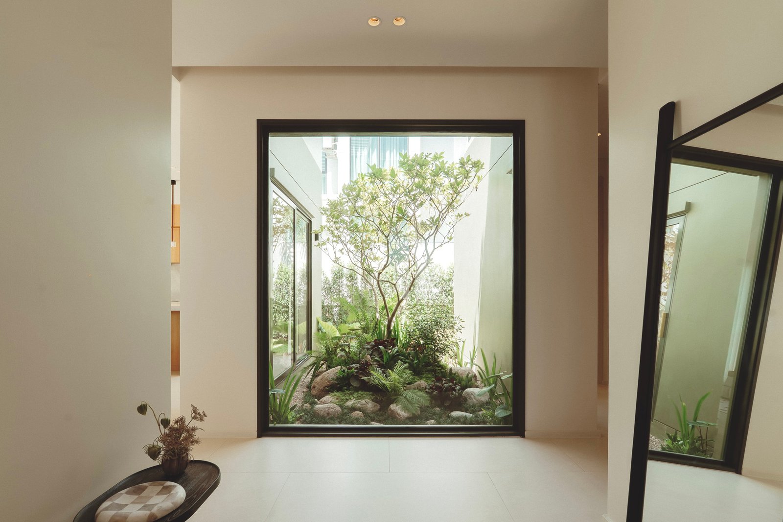Interior hallway opening to a bright glass-walled courtyard with a tree and greenery outside.
