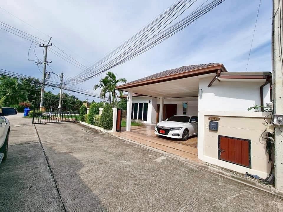 Single-story house with a covered carport; white sedan parked on a tiled driveway beside trimmed hedges.