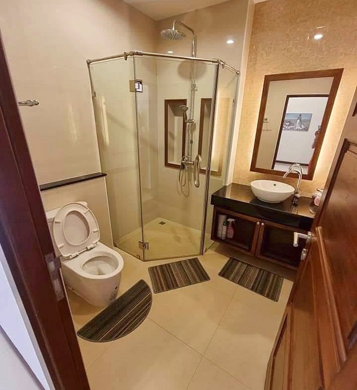 Modern bathroom with a glass corner shower, toilet to the left, and a dark wooden vanity with a round vessel sink and mirror above it.