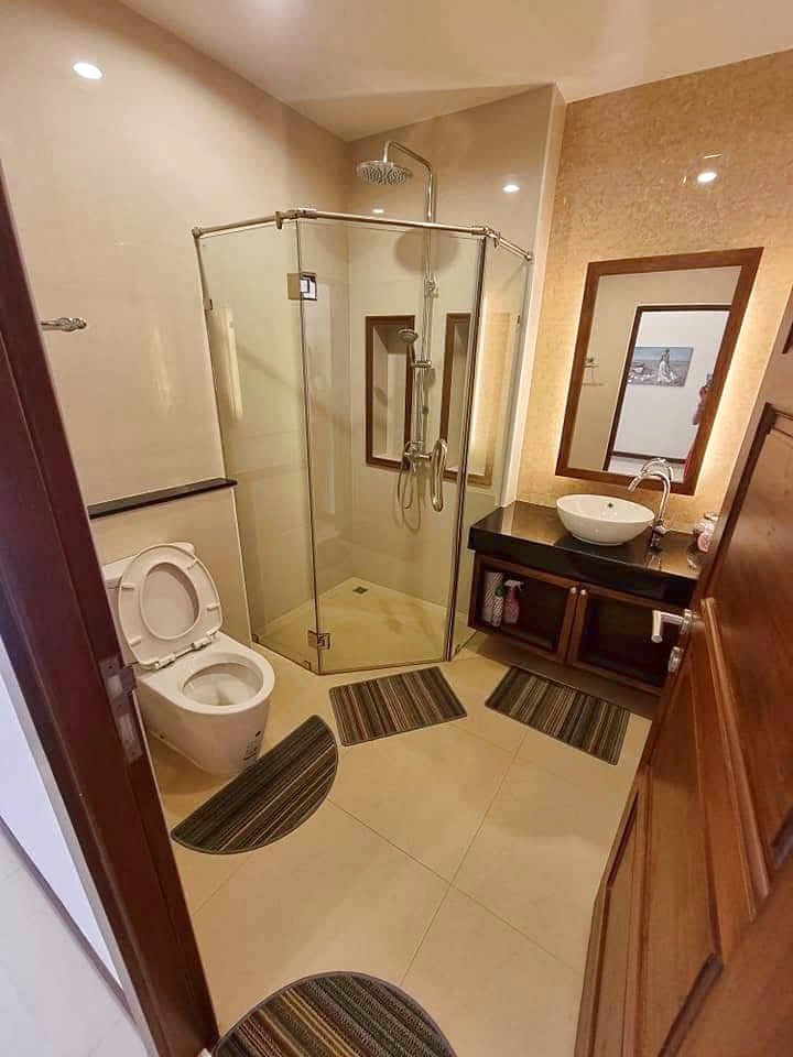 Garden_Ville_1_Pattaya_Rent_Rdl368_11 Modern bathroom with a glass corner shower, toilet to the left, and a dark wooden vanity with a round vessel sink and mirror above it.