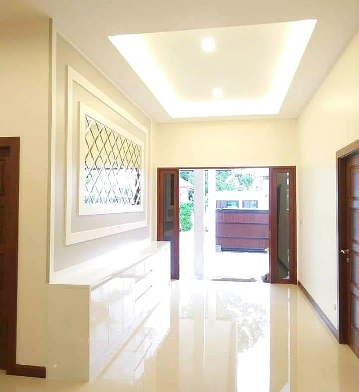 Bright, modern hallway with a glossy white floor, built-in white cabinet, decorative lattice window, and open French doors to outdoors.
