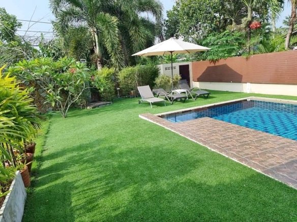 Backyard with a blue tiled swimming pool green lawn and white patio umbrella with lounge chairs nearby