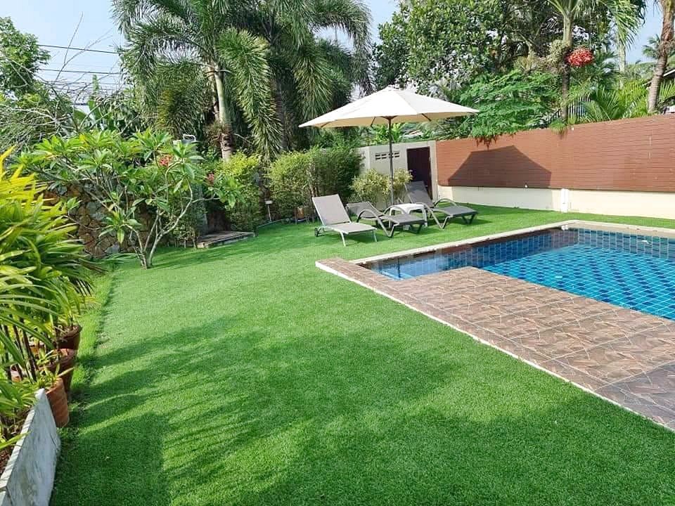 Backyard with a blue tiled swimming pool green lawn and white patio umbrella with lounge chairs nearby