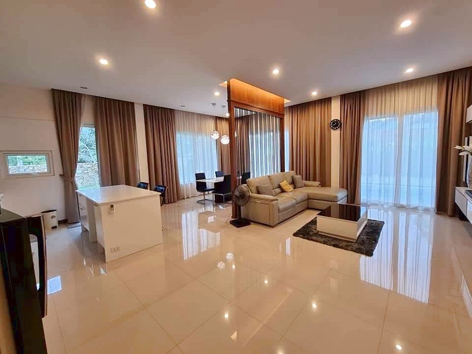 Open-concept living space with a cream sectional sofa, glass coffee table, and a white kitchen island under recessed lighting.
