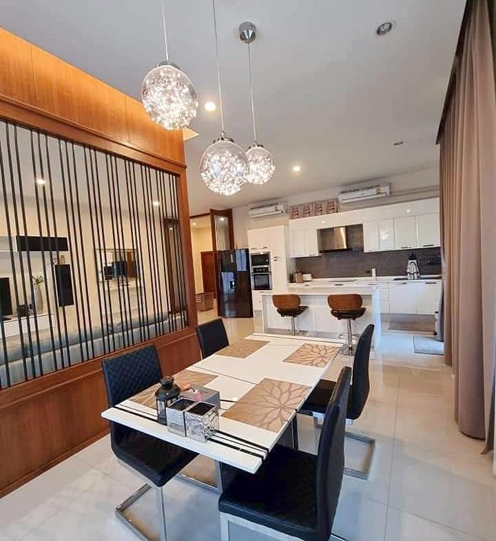 Modern dining area with glass pendant lights above a white striped table and black chairs, open kitchen in back.
