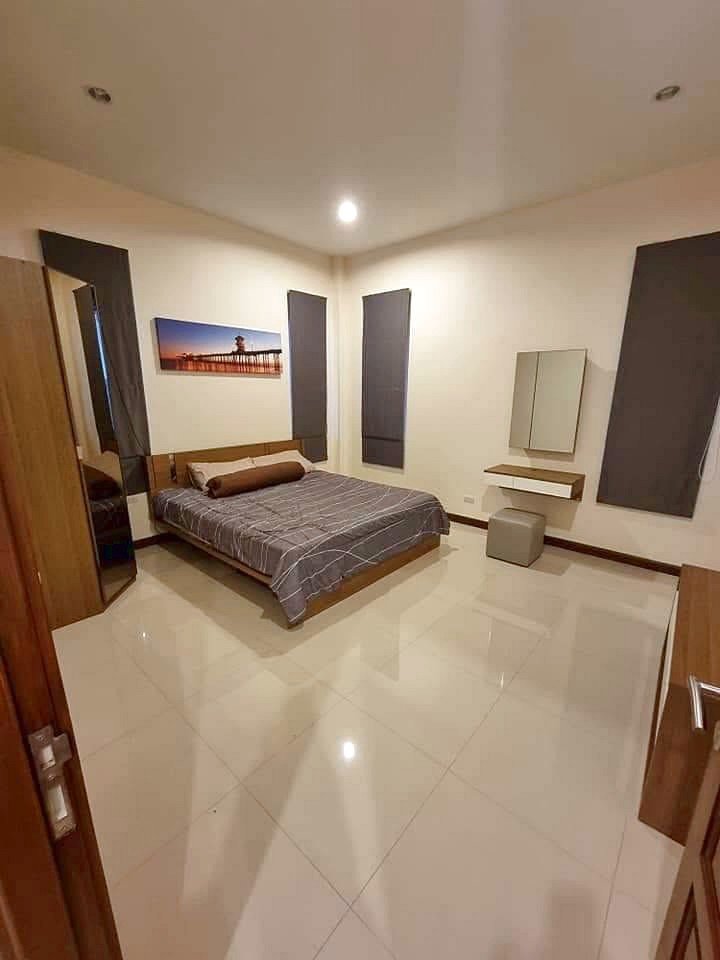 Garden_Ville_1_Pattaya_Rent_Rdl368_6 Modern bedroom with a wooden bed, gray striped bedding, and a brown bolster pillow, plus a wardrobe and wall art of a pier above the headboard.