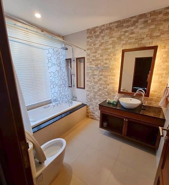 A modern bathroom with a bathtub along a window and a frosted glass shower curtain, plus a toilet in the foreground.