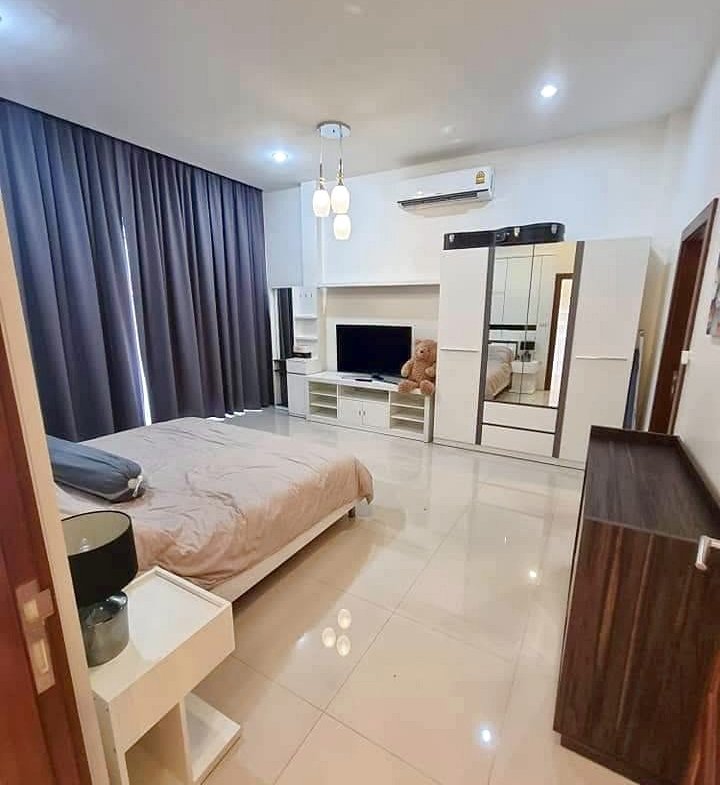 Modern bedroom with a low bed, beige bedding, dark floor-to-ceiling curtains, and glossy white tiled floor.