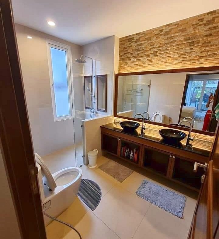 Modern bathroom with double sinks, large mirror, and glass shower; stone accent wall above the vanity.