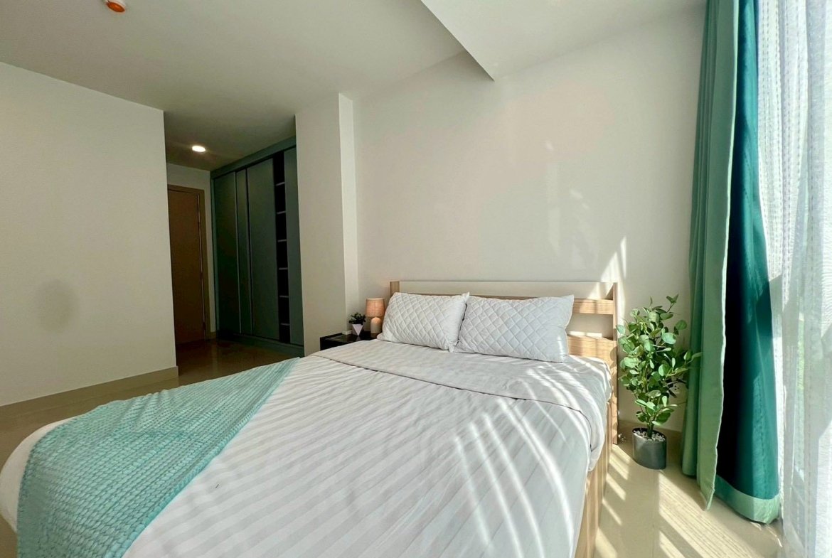 Bright, minimalist bedroom with a wooden bed, white striped bedding, turquoise throw, and a potted plant by the window.