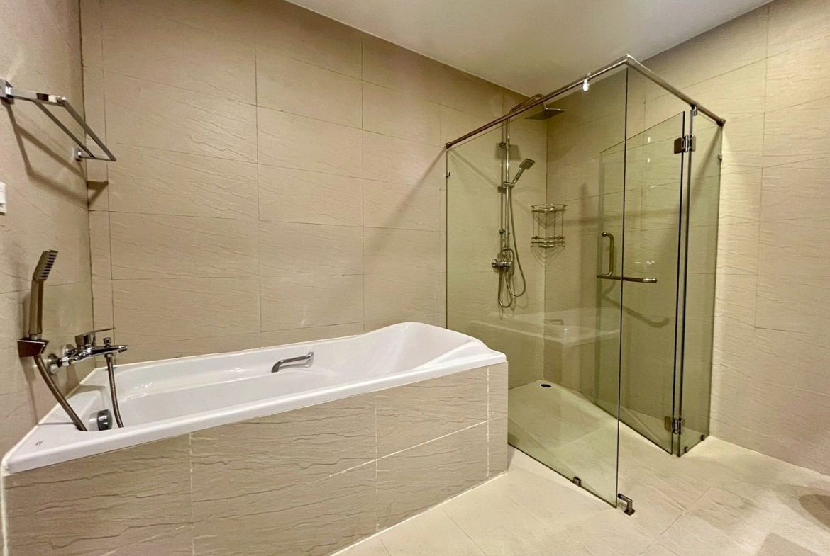 Modern beige-tiled bathroom with a white corner bathtub and a glass-walled shower enclosure.