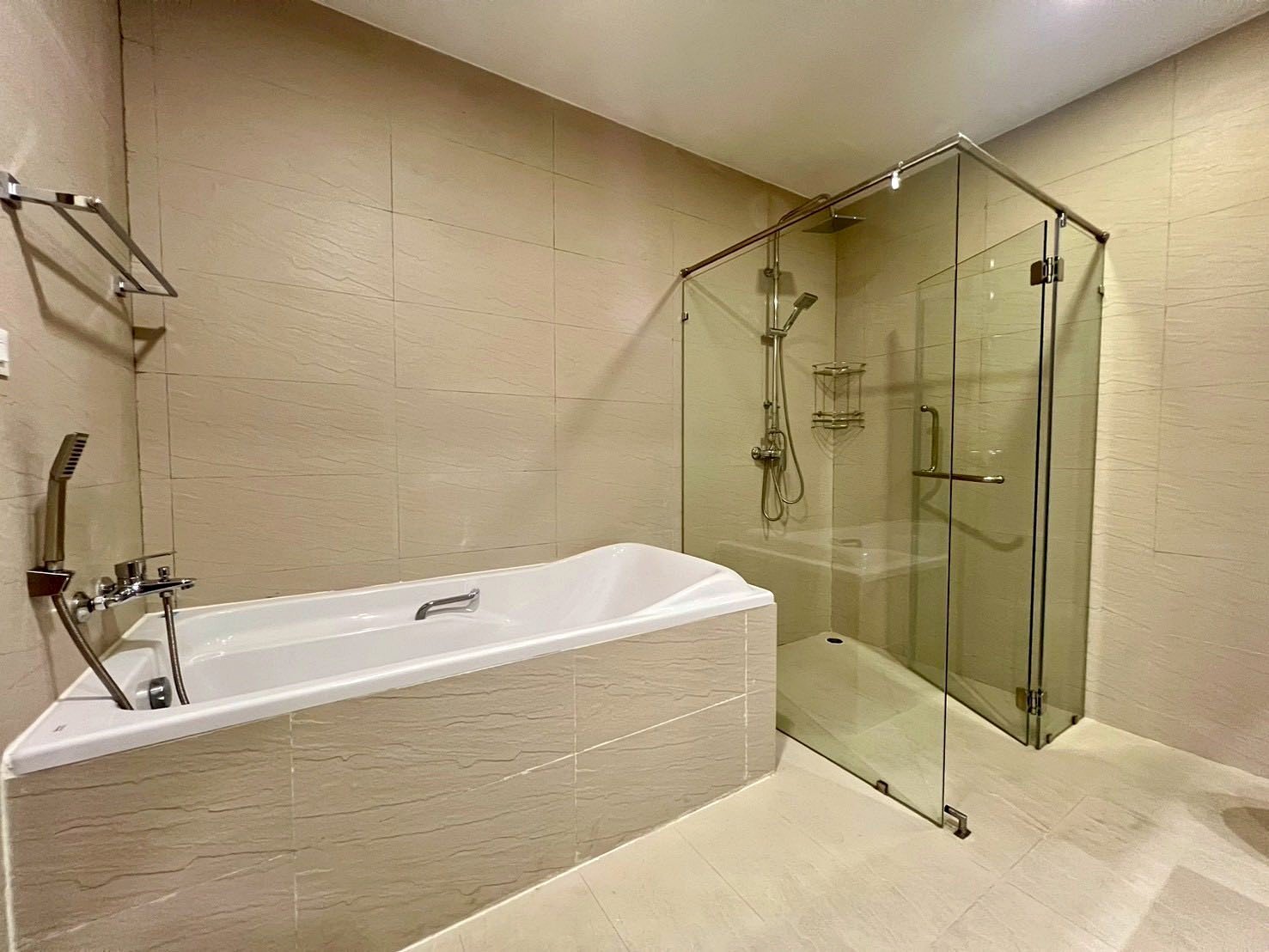 Gardenia_Pattaya_4Bed_Dlc492_19 Modern beige-tiled bathroom with a white corner bathtub and a glass-walled shower enclosure.