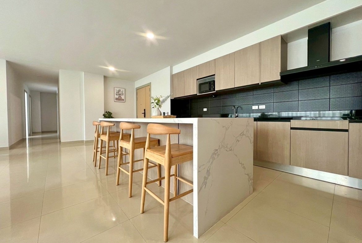 Modern open kitchen with a marble island and four wooden bar stools, light wood cabinets, and a black tiled backsplash.