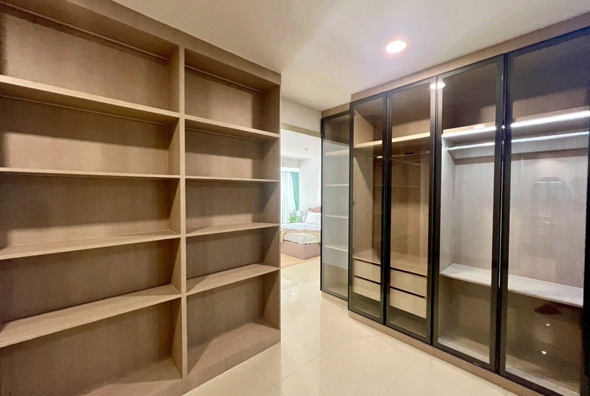 Walk-in closet with tall built-in wooden shelves on the left and glass-front wardrobes on the right, reflecting a modern, organized space.