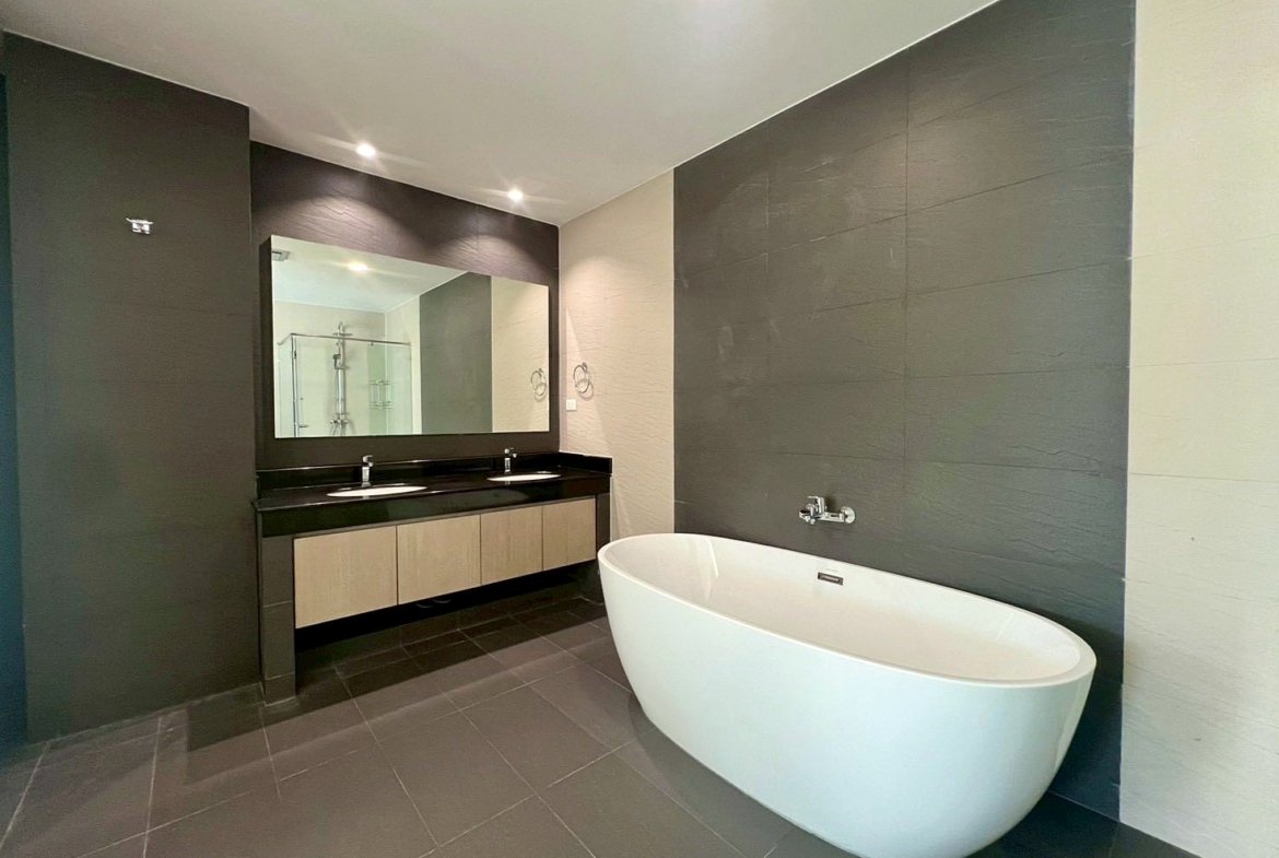 Contemporary bathroom with a white freestanding oval tub, dark tiled walls, and a double-sink vanity with a large mirror.