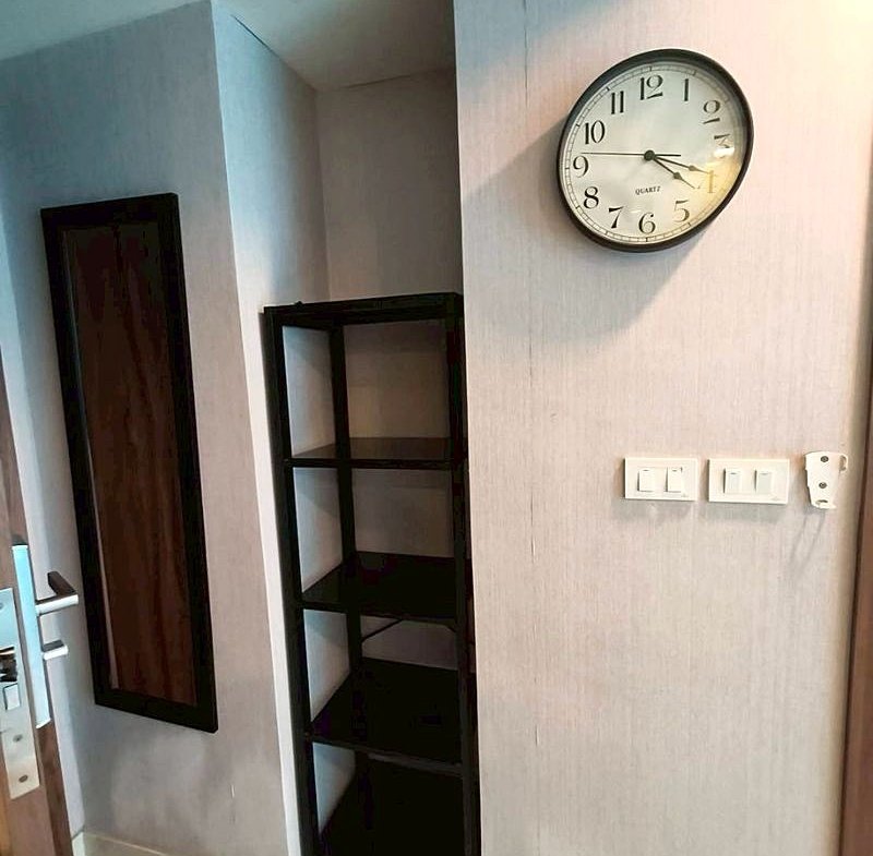 Interior hallway with a round wall clock, a tall black open-shelf unit, and a wall mirror beside the door