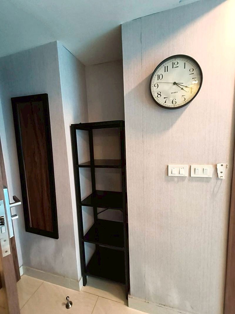 Grand_Avenue_Pattaya_Sale_Dlc641_10 Interior hallway with a round wall clock, a tall black open-shelf unit, and a wall mirror beside the door