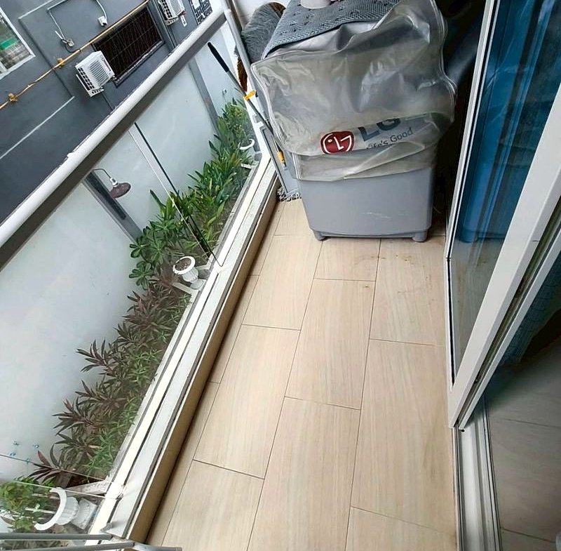 Narrow balcony storage area with a gray LG bag on a cabinet, a pink tub on top, and potted plants along a glass railing.