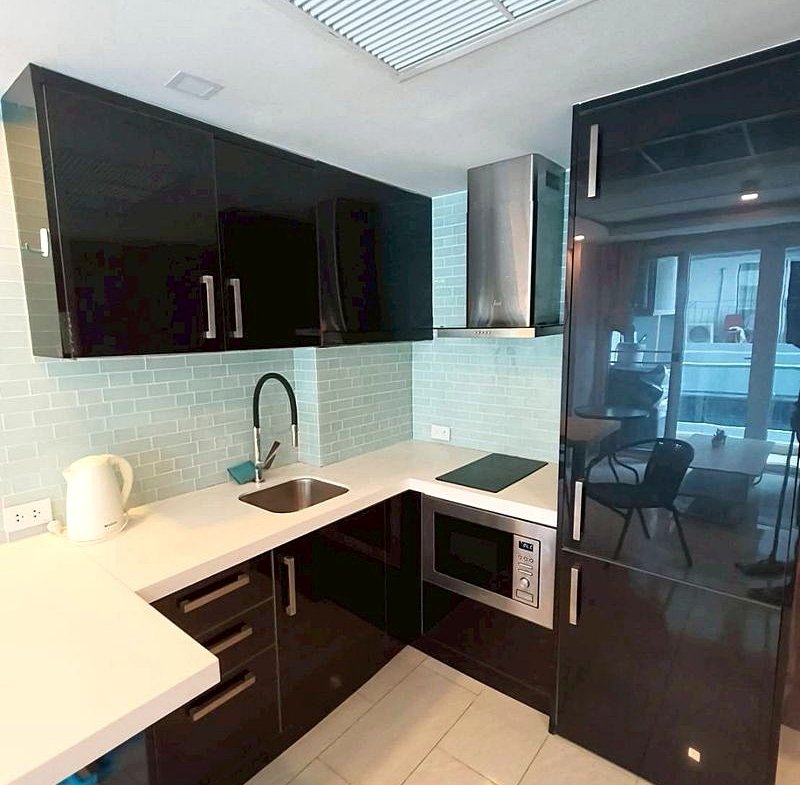 Modern L-shaped kitchen with glossy black cabinets, white countertop, light blue subway tile backsplash, and stainless steel range hood and microwave.