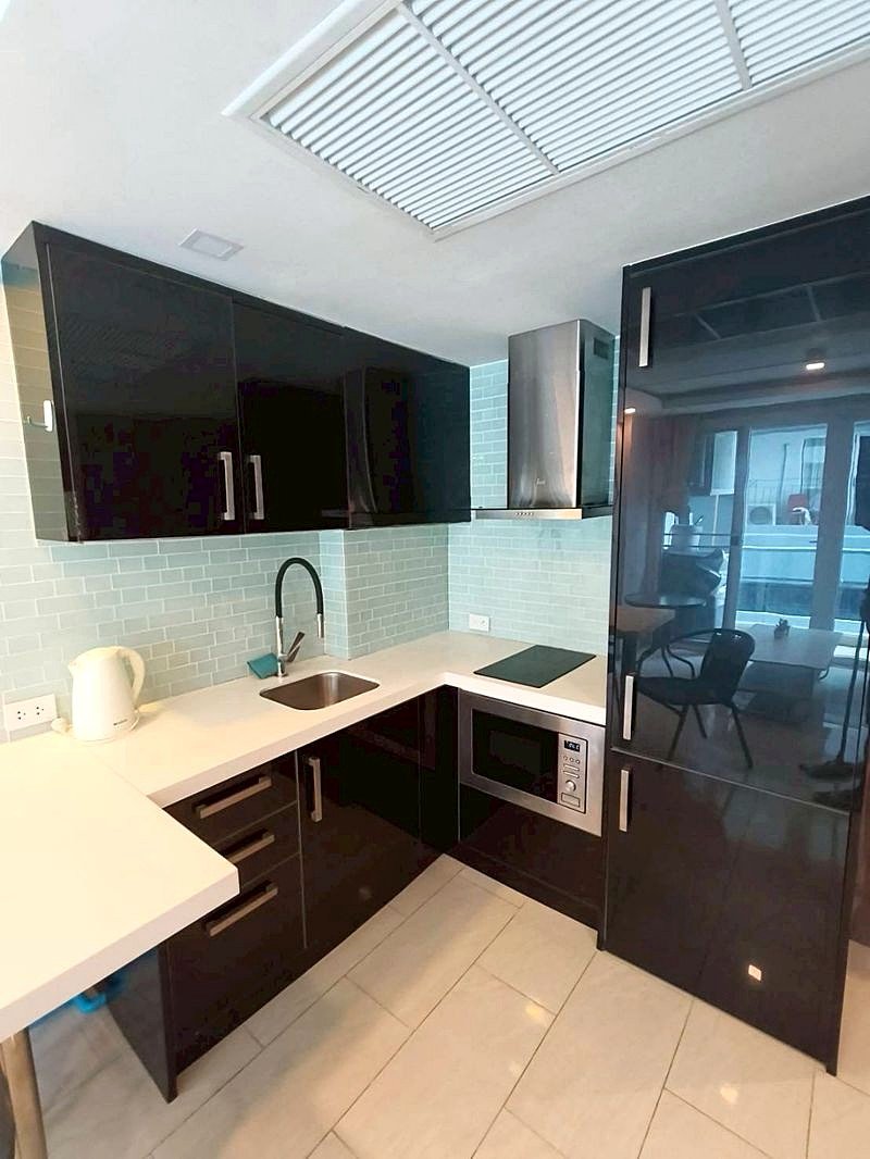 Grand_Avenue_Pattaya_Sale_Dlc641_2 Modern L-shaped kitchen with glossy black cabinets, white countertop, light blue subway tile backsplash, and stainless steel range hood and microwave.