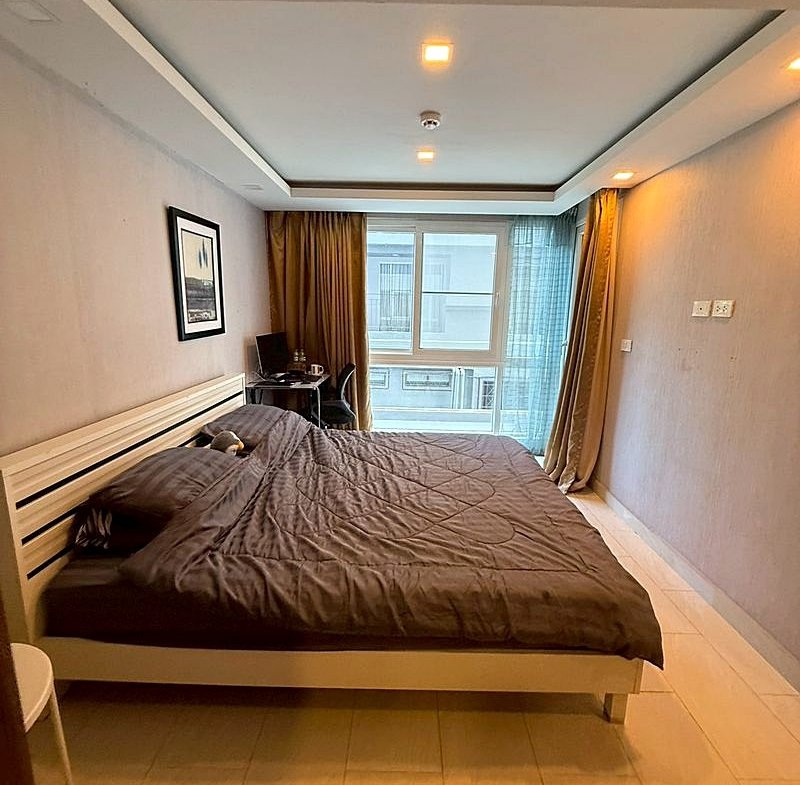 Bedroom with a large bed in dark gray bedding, white slatted headboard, and a window with gold and blue curtains.