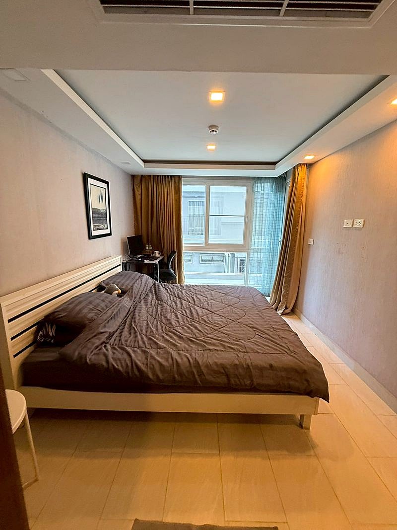 Grand_Avenue_Pattaya_Sale_Dlc641_3 Bedroom with a large bed in dark gray bedding, white slatted headboard, and a window with gold and blue curtains.