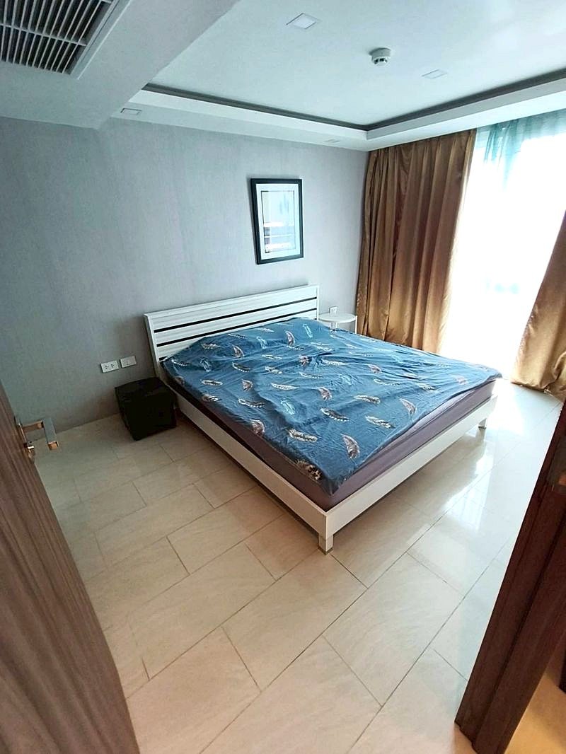 Grand_Avenue_Pattaya_Sale_Dlc641_4 Modern bedroom with a white platform bed, blue feather-pattern sheets, a framed wall art, and a white nightstand beside it.