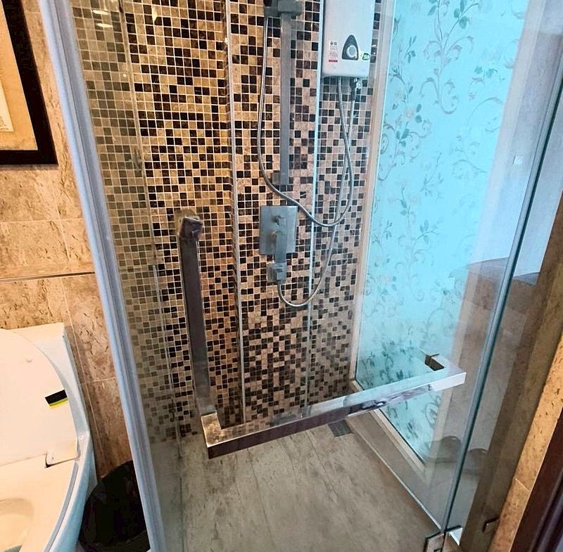 Shower stall with mosaic tile wall, glass door, and a handheld shower head on a flexible hose with a chrome grab bar inside.