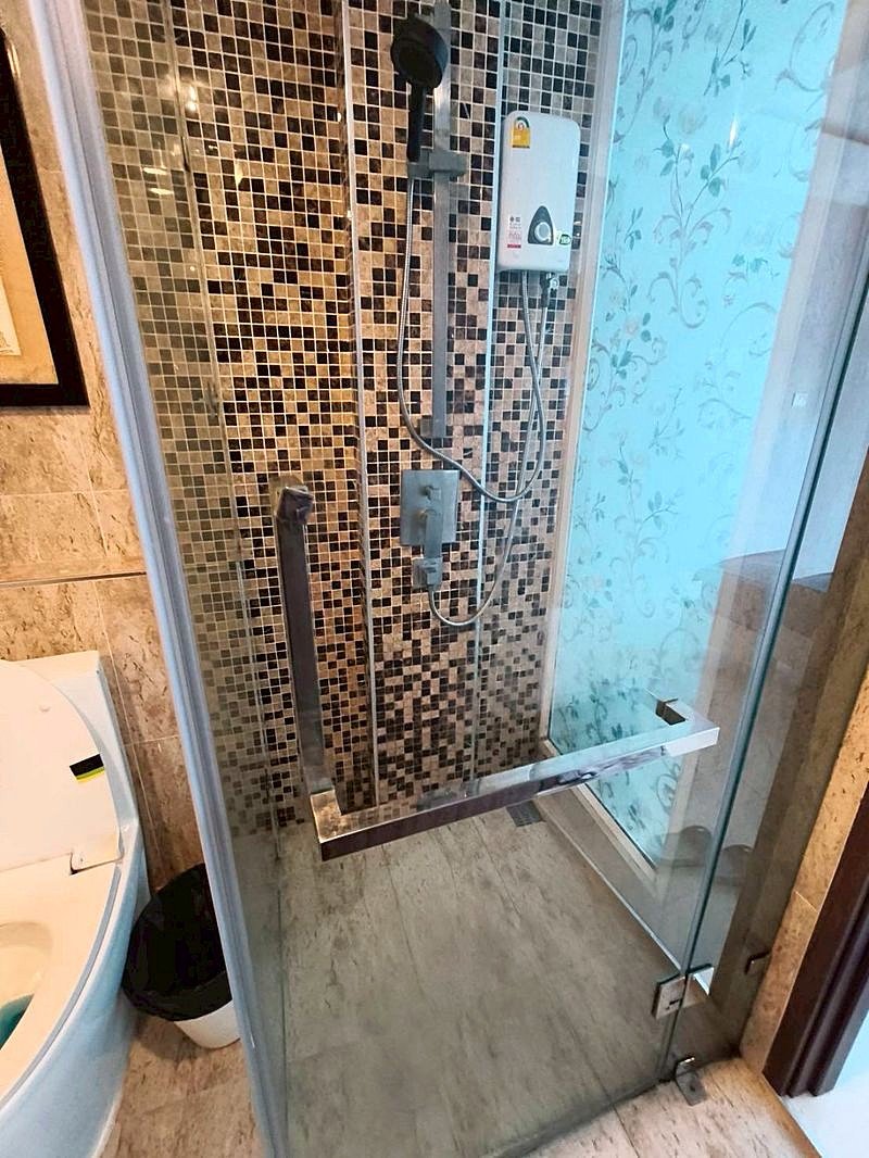 Grand_Avenue_Pattaya_Sale_Dlc641_6 Shower stall with mosaic tile wall, glass door, and a handheld shower head on a flexible hose with a chrome grab bar inside.