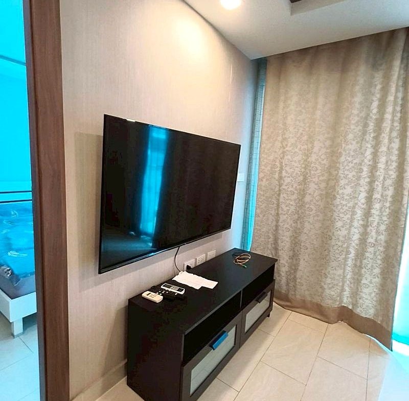 Flat-screen TV mounted on a light wall above a dark TV console with remotes and papers nearby.