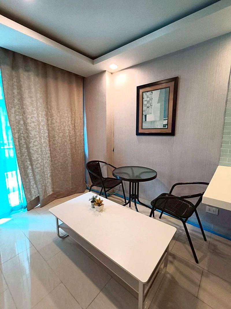 Grand_Avenue_Pattaya_Sale_Dlc641_9 Cozy seating nook with a white coffee table, two black chairs, and a small round glass table against a textured wall and framed artwork.