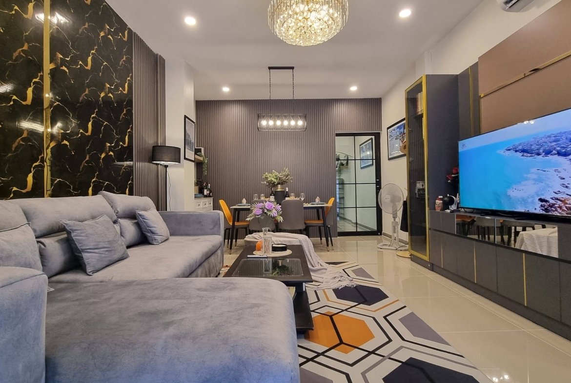 Open-concept living room with a gray sectional, geometric rug, and a marble-accent wall; dining area in the background.