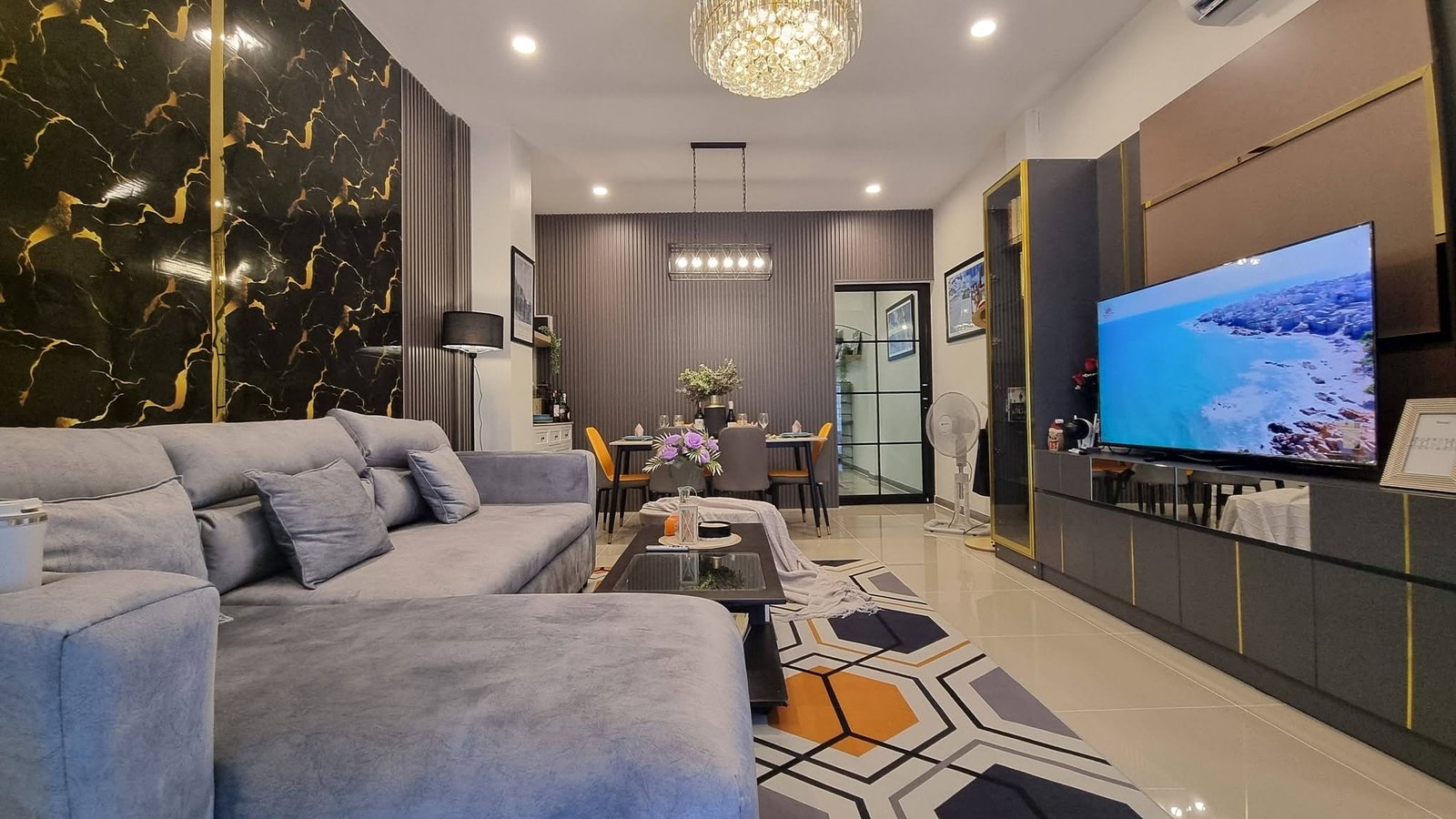 Open-concept living room with a gray sectional, geometric rug, and a marble-accent wall; dining area in the background.