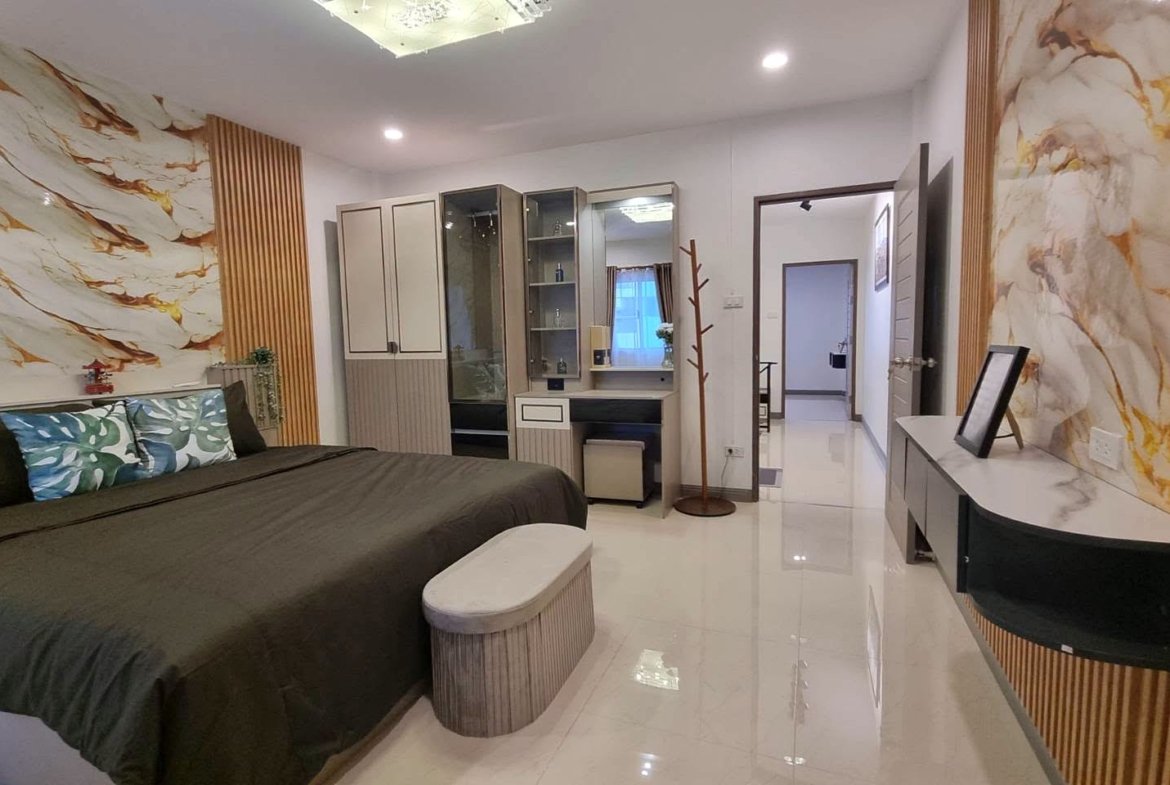 A modern hotel-style bedroom with a large bed, olive bedding, marble-patterned walls, and wooden slat accents on either side of the wall.
