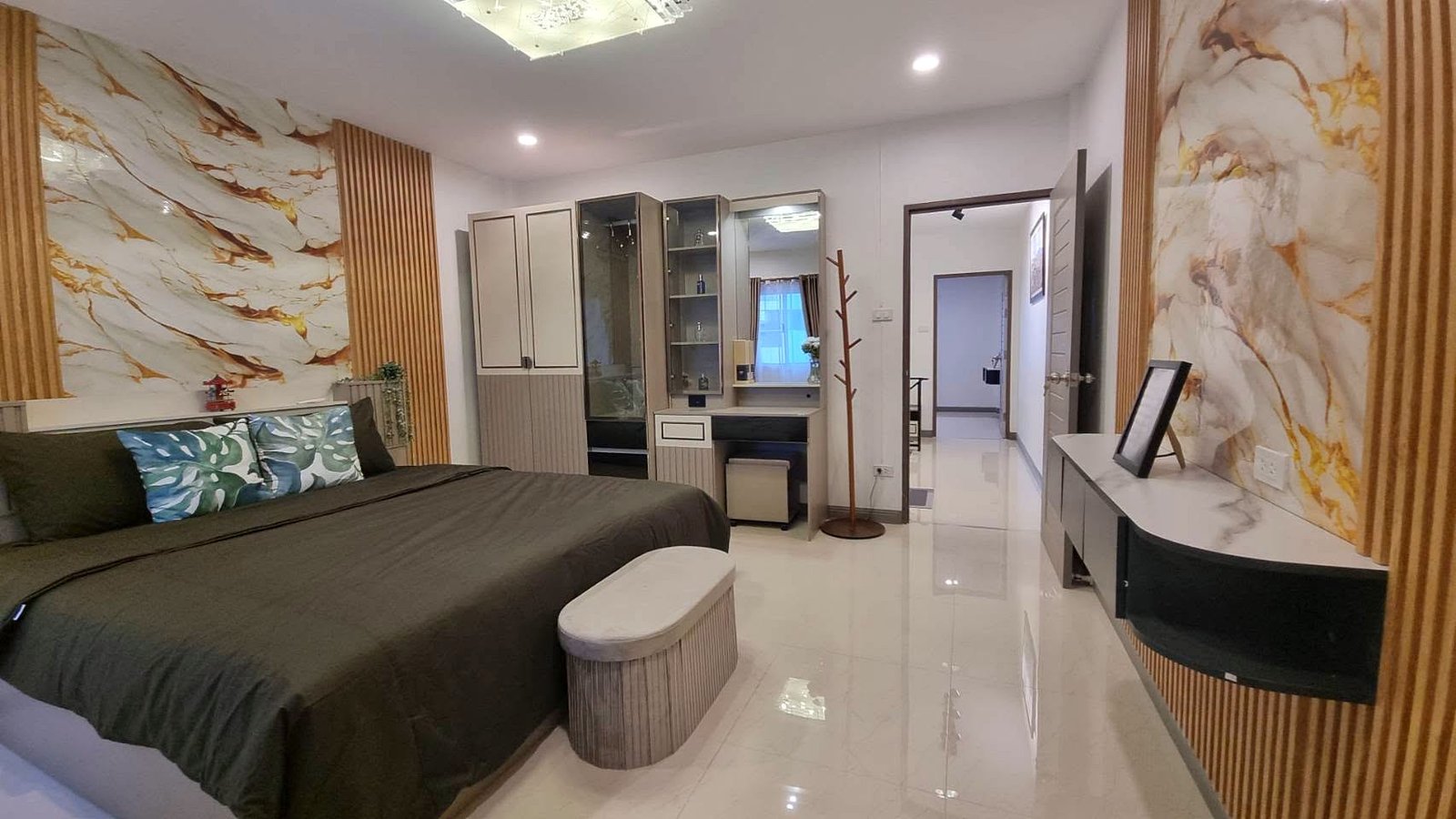 A modern hotel-style bedroom with a large bed, olive bedding, marble-patterned walls, and wooden slat accents on either side of the wall.