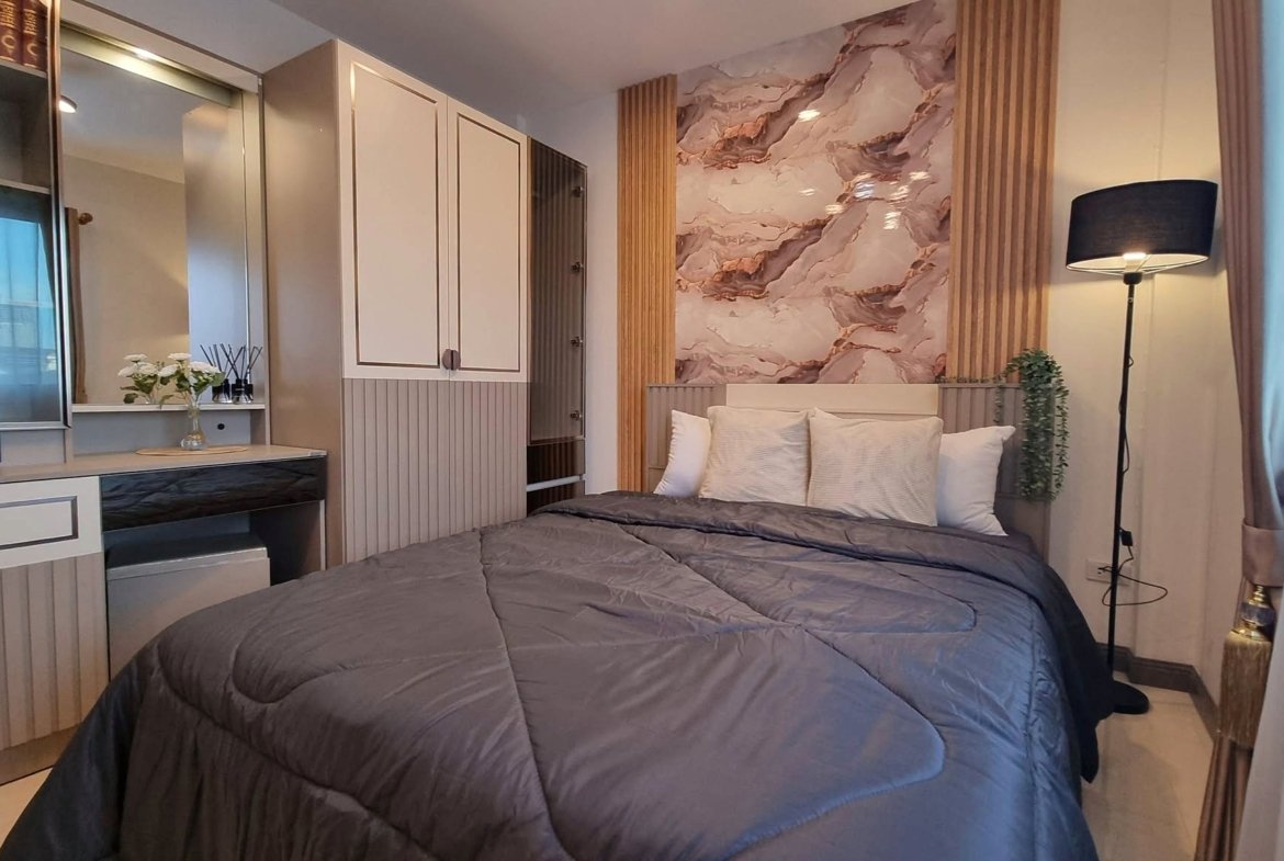 Cozy modern bedroom with a large gray quilted bed, marble wall art, and built-in cream cabinets on the left.