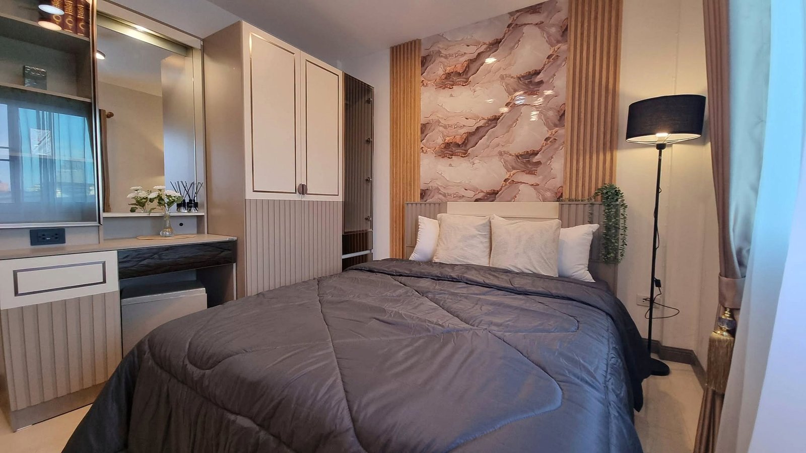 Cozy modern bedroom with a large gray quilted bed, marble wall art, and built-in cream cabinets on the left.