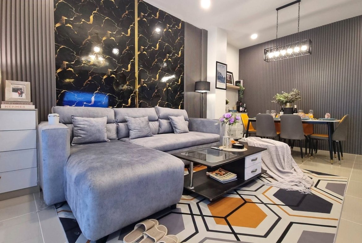 Open-concept living room with a grey sectional sofa, a black-and-gold marble accent wall, and a dining area nearby.