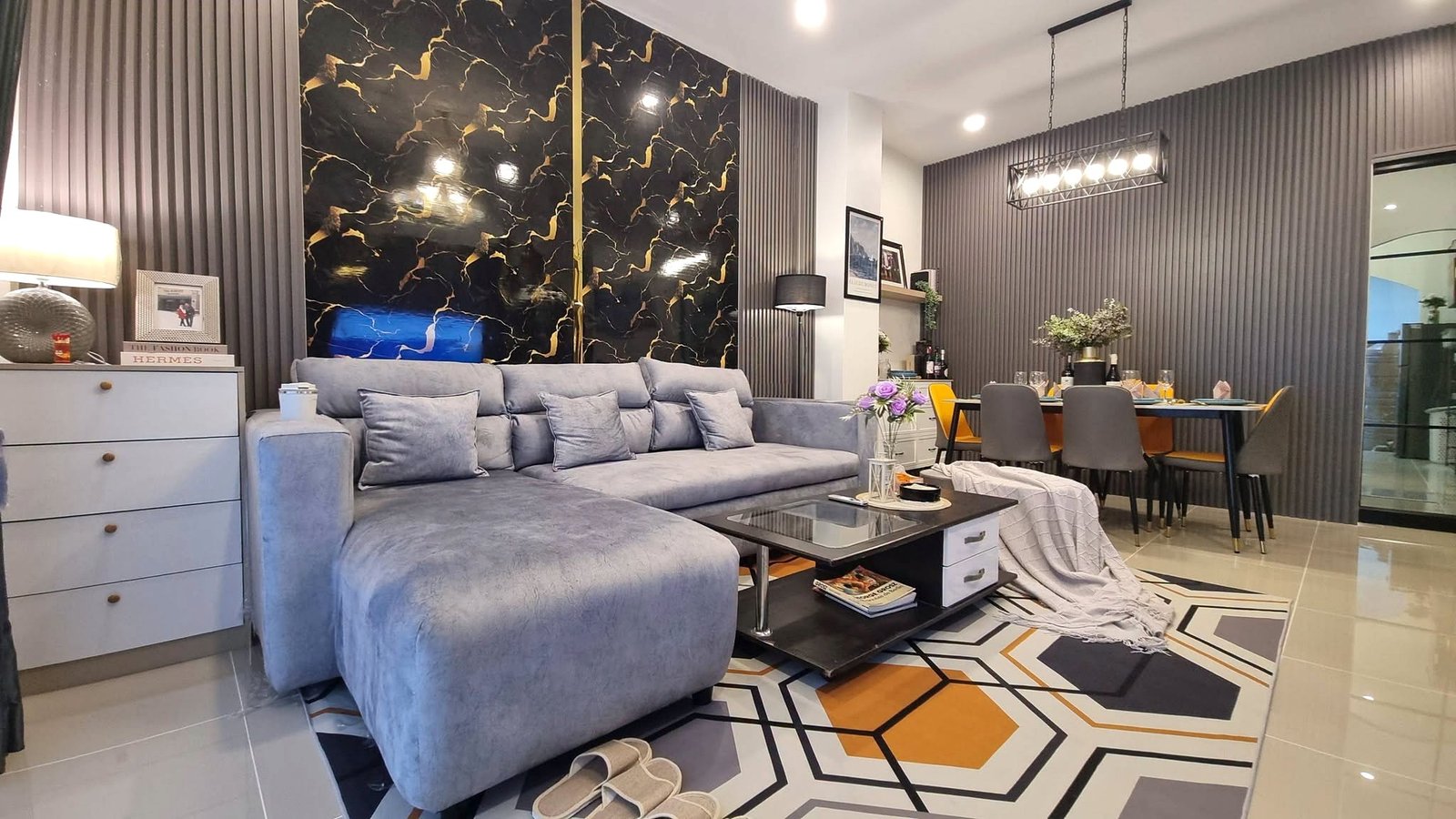 Open-concept living room with a grey sectional sofa, a black-and-gold marble accent wall, and a dining area nearby.