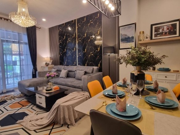 Open plan living and dining area with a crystal chandelier gray sectional sofa marble pattern feature wall and a dining table set with turquoise plates and yellow chairs