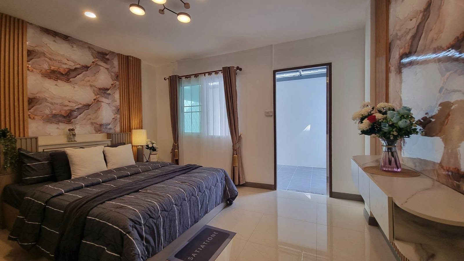 King bed with dark gray quilt and white pillows, marble-patterned walls, and warm bedside lighting in a modern bedroom