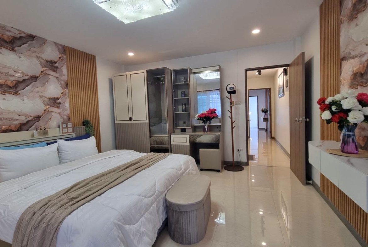 Modern bedroom with a large white bed, marble-patterned walls, wooden vertical accents, and a vanity area along the back wall.
