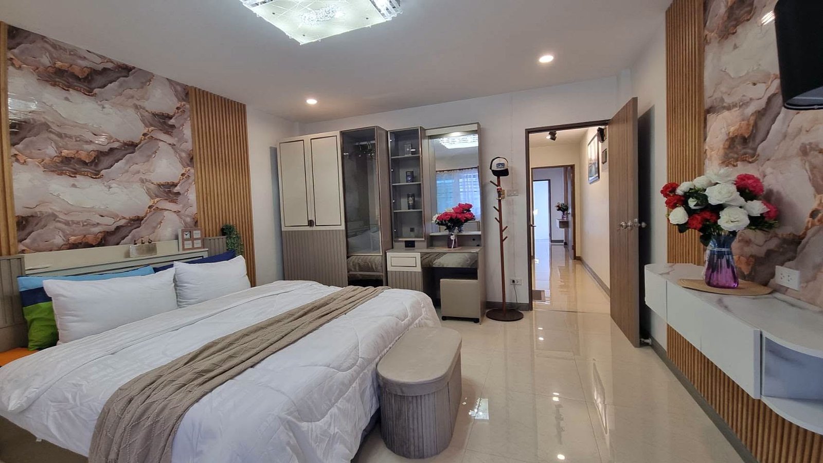 Modern bedroom with a large white bed, marble-patterned walls, wooden vertical accents, and a vanity area along the back wall.