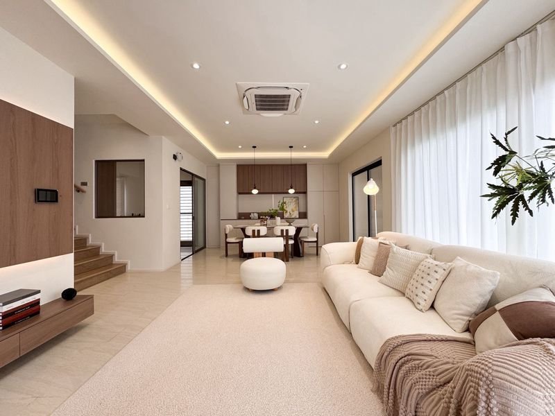 Open plan living room and dining area with a cream sectional sofa white ottoman and a beige rug large glass doors with sheer curtains and a potted plant on the right