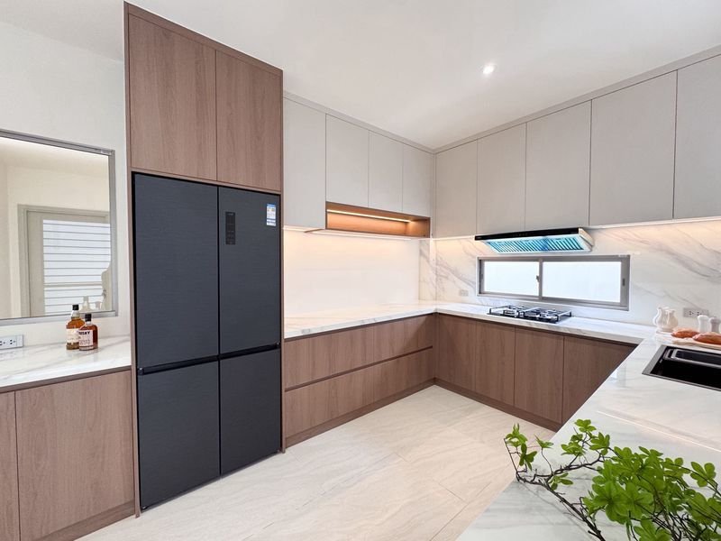 Modern U-shaped kitchen with light wood lower cabinets, white upper cabinets, and a large black–gray refrigerator centerpiece.