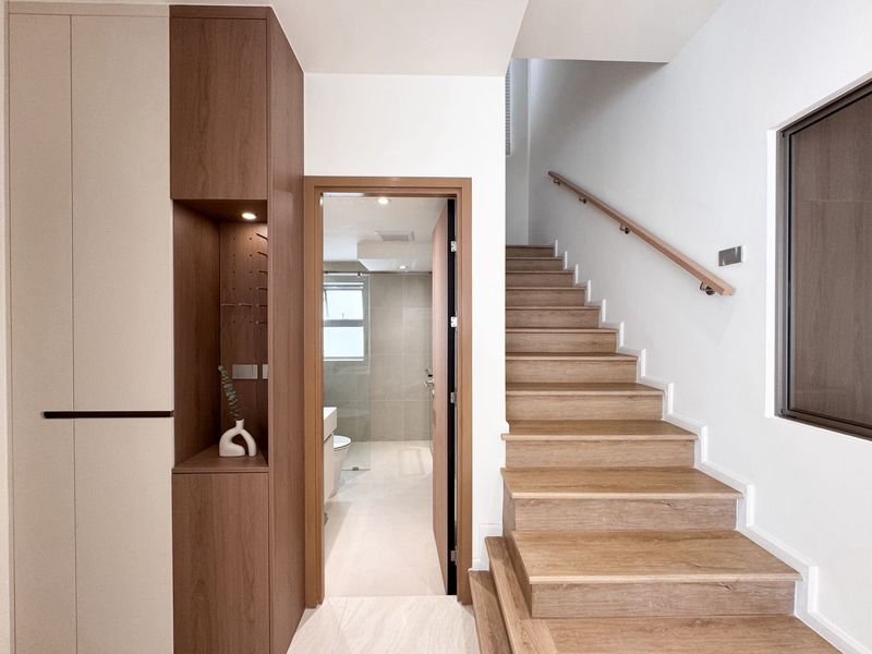 Modern entry hall with built-in wooden storage on the left, open bathroom door straight ahead, and a wooden staircase to the right.