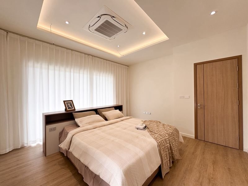 Modern bedroom with a large white bed, beige bedding, and a wooden headboard under recessed ceiling lights.