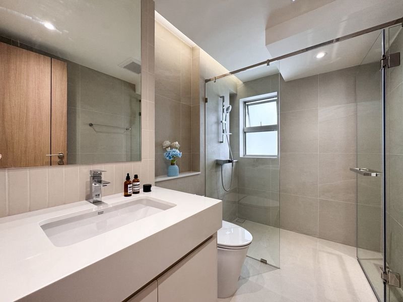 Modern bathroom with white vanity, rectangular sink, glass-enclosed shower, toilet, and a small window.
