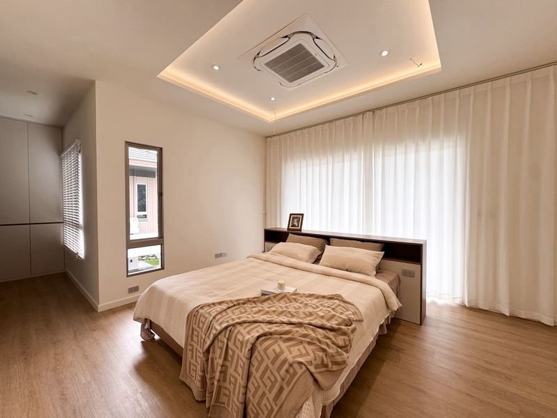 Modern minimalist bedroom with a low bed, beige bedding, and sheer white curtains along a large window.